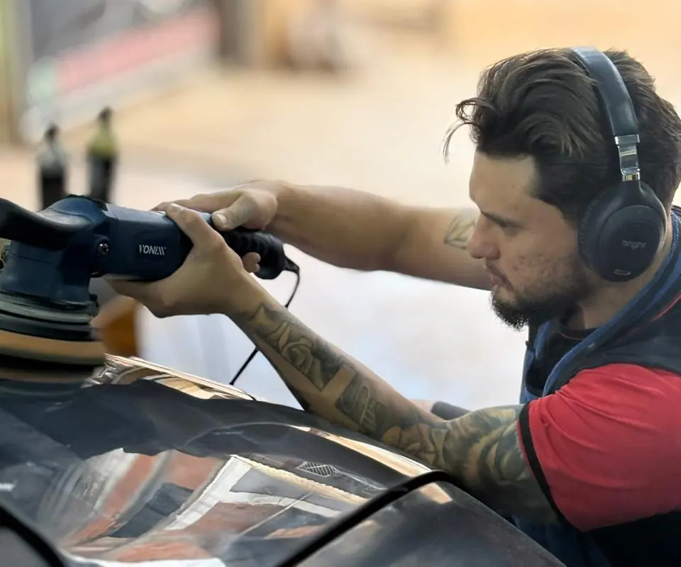 Polimento em andamento com politriz no capô de um carro